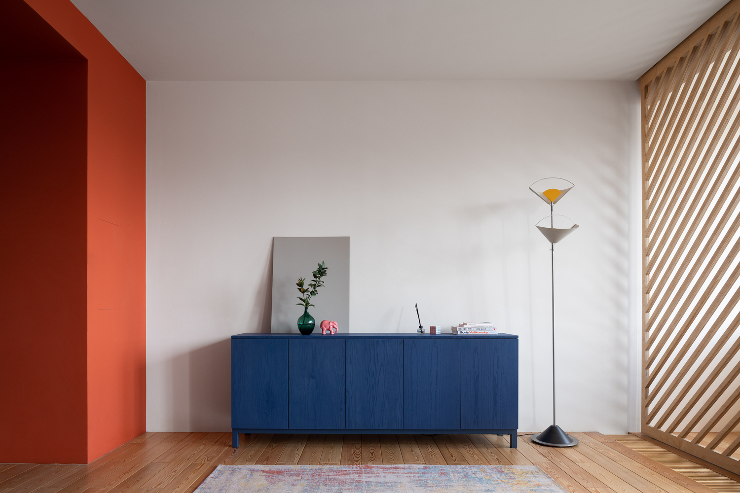 Tủ lưu trữ sơn màu xanh lam đậm đối diện khu vực tiếp khách, nổi bật trên nền tường màu trắng và sàn gỗ tự nhiên ấm áp.