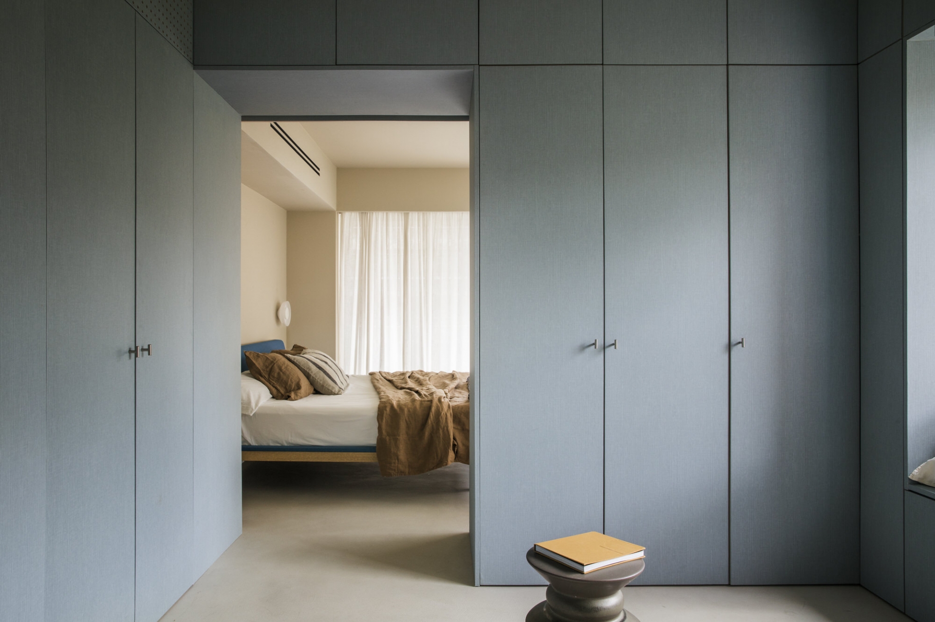 Xung quanh phòng ngủ chính của bố mẹ được thiết lập hệ thống tủ lưu trữ cao kịch trần với gam màu xanh xám thời trang. Giải pháp này giúp tối ưu hóa chiều cao trần, cho không gian luôn gọn gàng, ngăn nắp.
