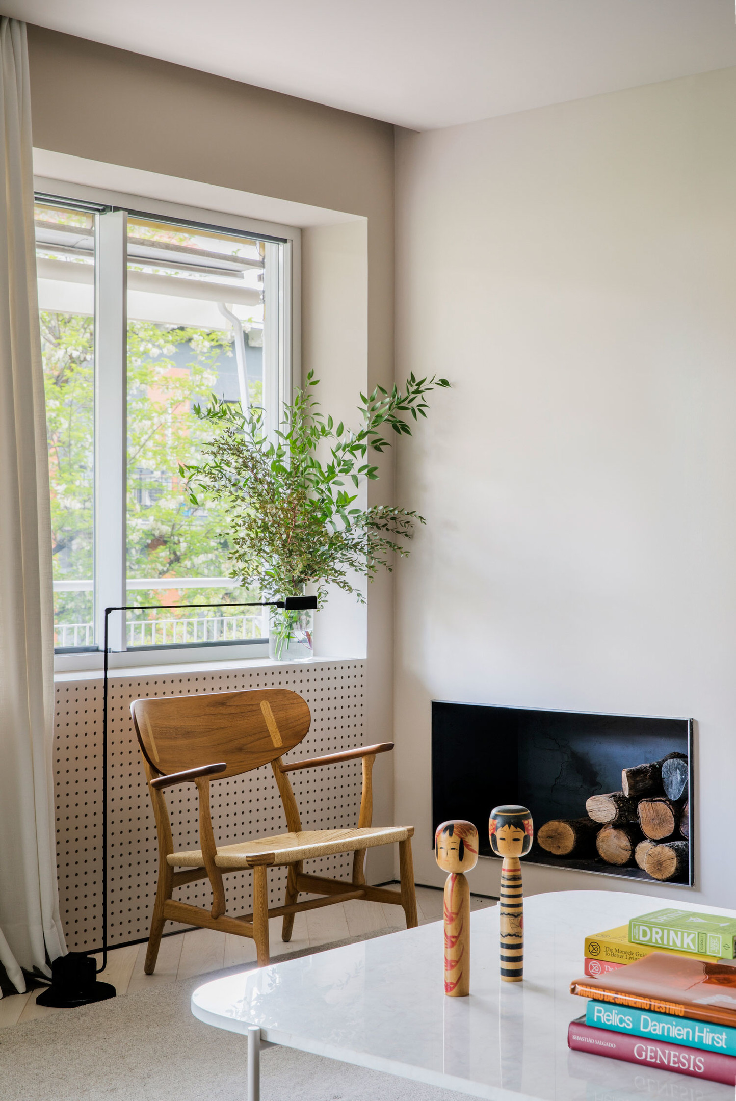 Bên cạnh ô cửa sổ, một chiếc ghế bành bằng gỗ nhỏ nhắn với chiếc đèn sàn có thể điều chỉnh độ cao khi chủ nhân cần đọc sách. Trên bệ cửa sổ là lọ hoa thủy tinh với những nhánh cây xanh tươi mắt. 