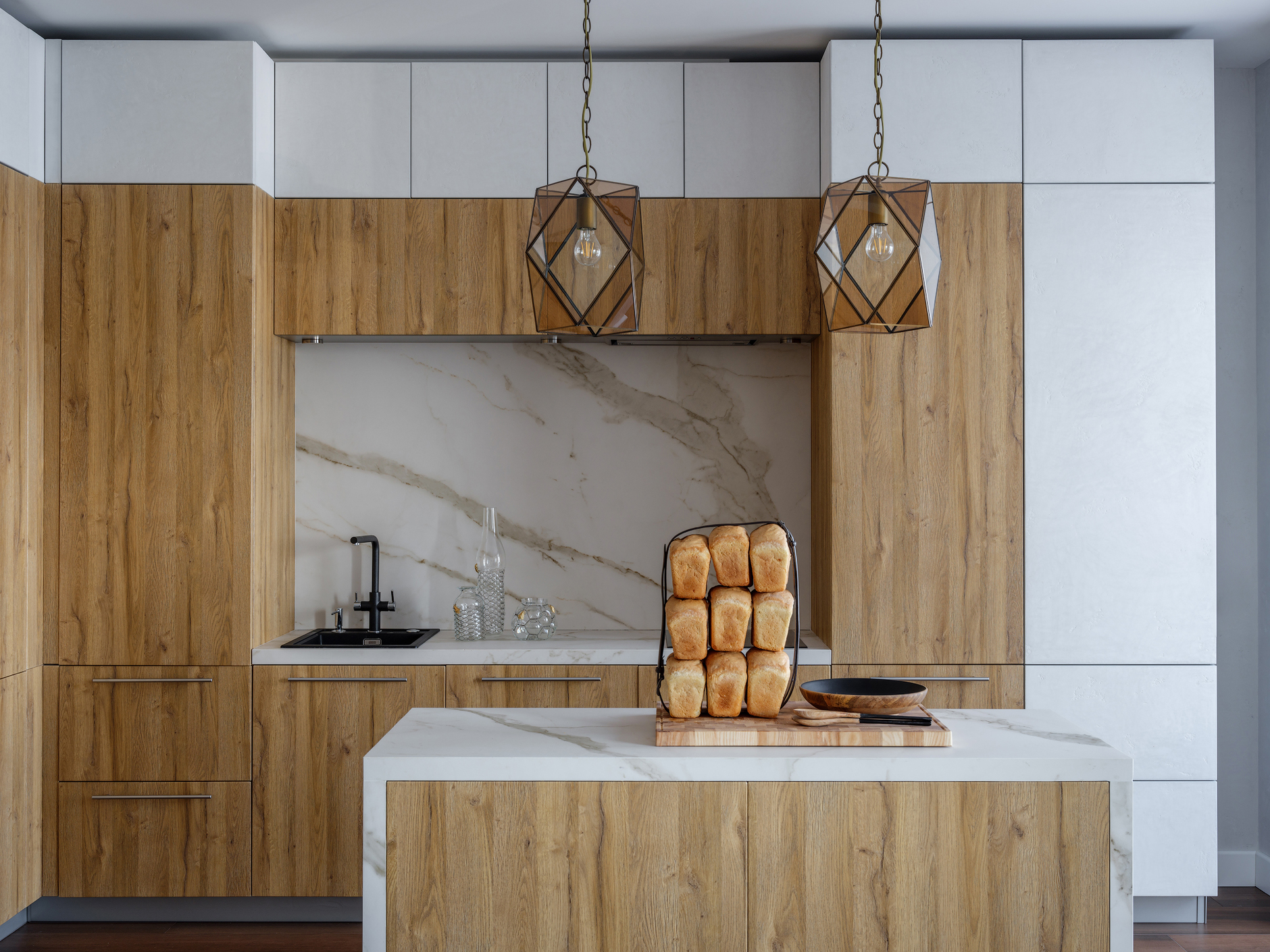 Phòng bếp là sự kết hợp hệ tủ lưu trữ màu xám và gỗ, tương đồng với sự phối màu của đảo bếp ở khu vực trung tâm. Những chiếc đèn thả trần phong cách cổ điển của Ý cùng với mặt bàn và khu vực backsplash ốp đá cẩm thạch càng thêm sang trọng.