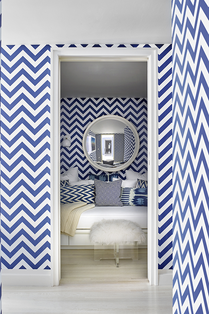 Hiệu ứng mà giấy dán tường màu xanh lam - trắng họa tiết zigzag cũng như tấm gương hình tròn lớn chính giữa bức tường phòng ngủ khiến không gian vốn nhỏ hẹp trong một hốc tường bỗng trở nên có chiều sâu hun hút đầy tính nghệ thuật.