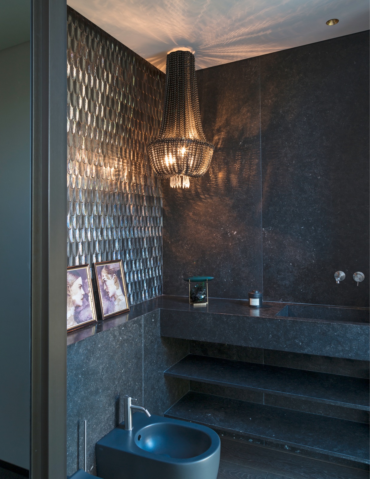 Thay vì sử dụng đèn chùm tại vị trí bồn tắm như thường thấy, NTK Eleanor Cavalli đã lựa chọn chiếc đèn chùm pha lê màu đen kết hợp ánh sáng vàng ấm ngay tại nhà vệ sinh, tạo nên một phong cách ấn tượng cho chủ sở hữu là quý ông độc thân.