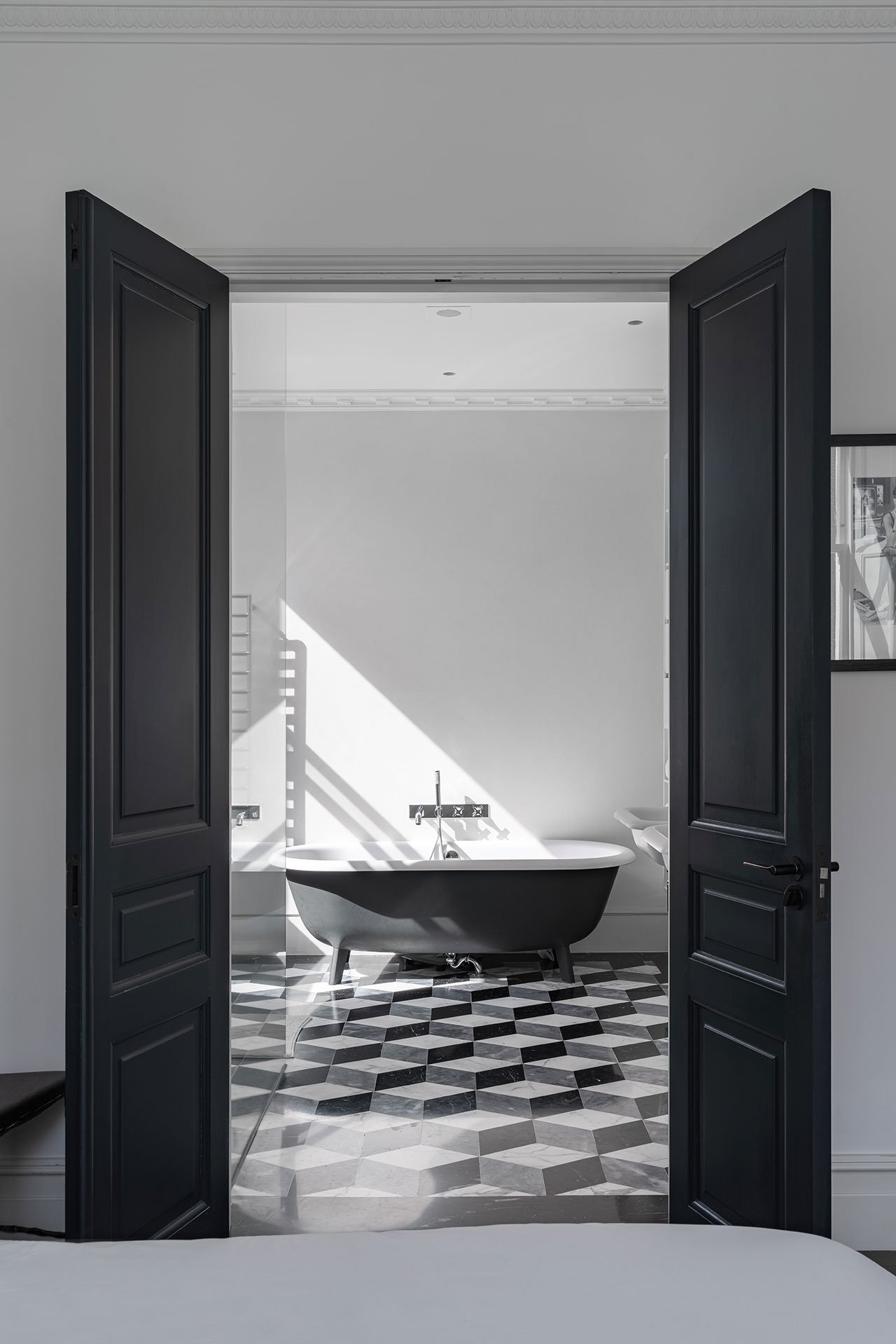 Bồn tắm nằm thiết kế cổ điển với gam màu trắng đen sang trọng, phối hợp hài hòa của cánh cửa đen - tường trắng, sàn nhà lát gạch trắng đen xám, kể cả bức ảnh bên ngoài cũng theo phong cách này.