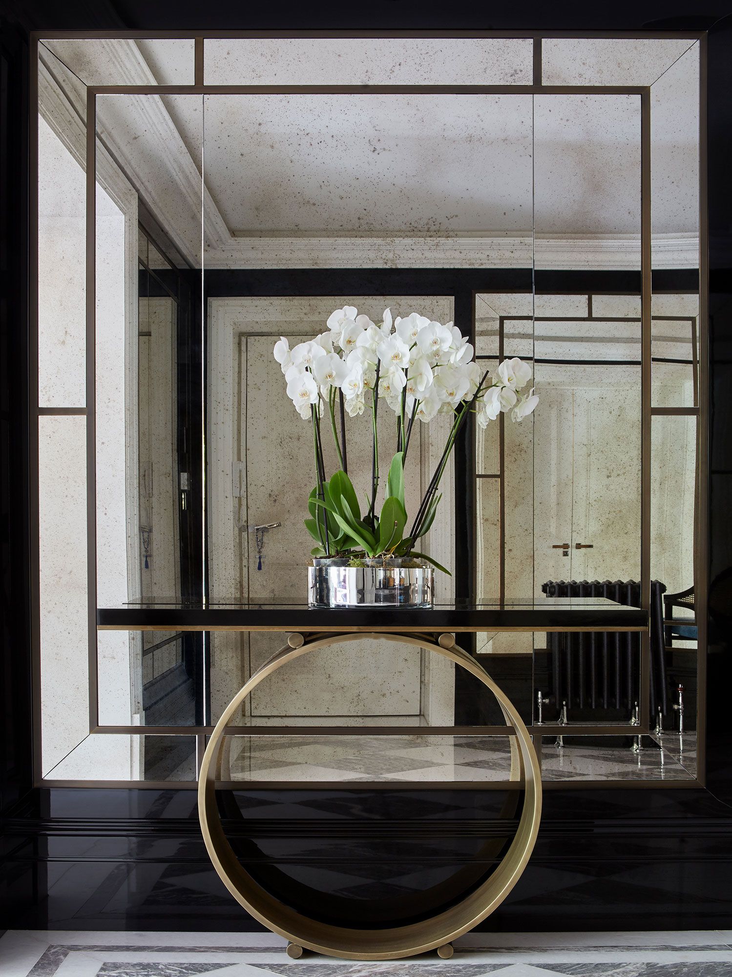 Lối vào căn hộ sang chảnh với tone đen huyền bí, kết hợp bàn gắn tường chân tròn cùng những bông hoa phong lan trắng muốt. Tấm gương 'full' ngay tường tại vị trí này cũng giúp bạn ngắm nhìn hết vẻ đẹp sang chảnh của hành lang phản chiếu từ nó.
