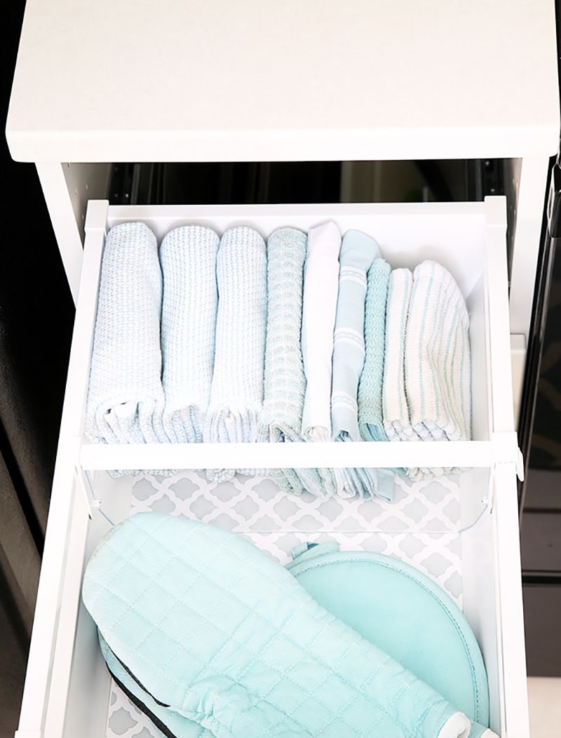 Hãy thử chọn một giải pháp tinh tế và kín đáo hơn, đó là gấp những chiếc khăn gọn gàng rồi xếp thành thứ tự theo chiều ngang trong hộc tủ bếp.