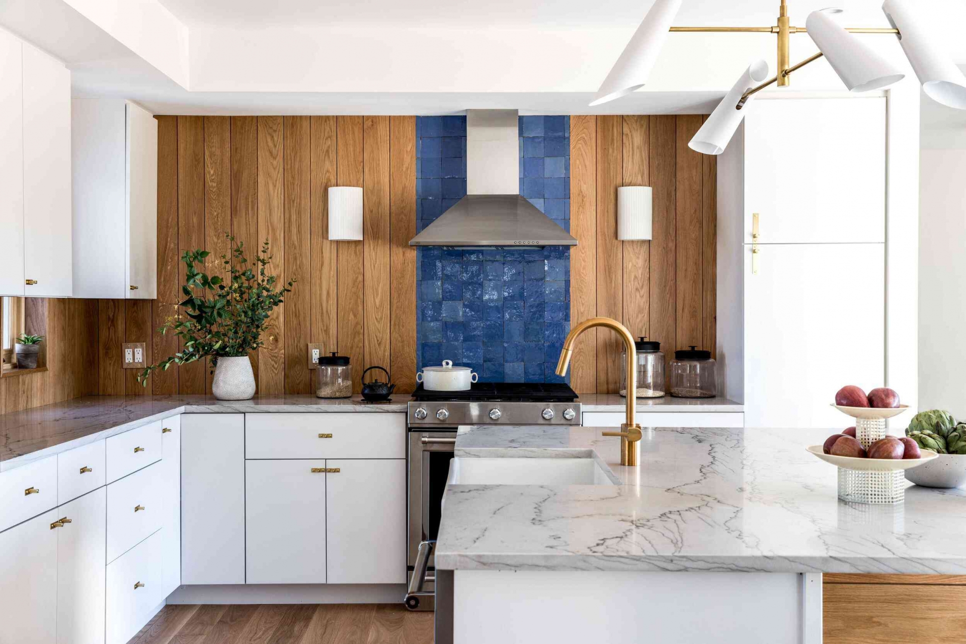 Bức tường trong phòng bếp thay vì chỉ sử dụng gạch màu xanh coban lấp lánh ngay sau bếp nấu thì nhà thiết kế đã lựa chọn vật liệu gỗ ốp dọc quanh khu vực backsplash vừa để tạo chiều sâu cho bếp màu trắng vừa giúp sắc xanh nổi bật hơn.