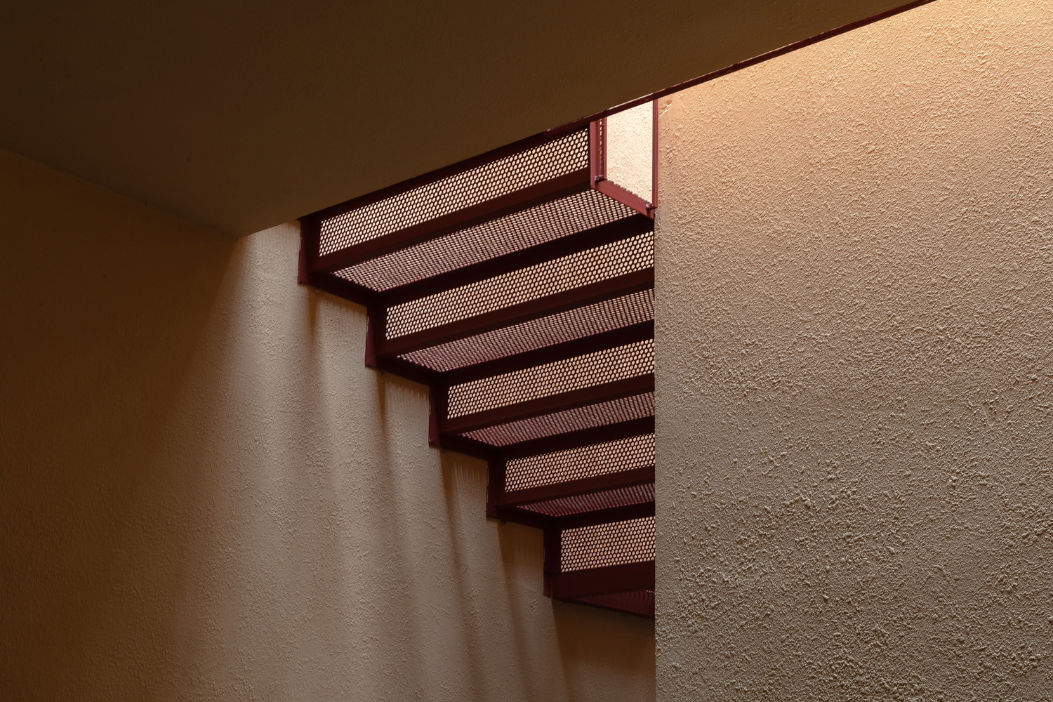 Cầu thang với lan lan và những bậc tam cấp đỏ thiết kế dạng lưới kim loại cho phép ánh sáng xuyên suốt cầu thang từ tầng trên cao xuống đến không gian bên dưới, kết hợp với ánh nắng tạo nên những khoảng không đầy tính nghệ thuật.