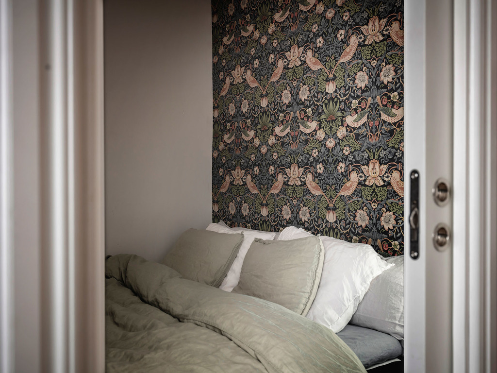 Phòng ngủ tuy nhỏ nhưng không vì thế mà thiếu đi cá tính. Khu vực đầu giường sử dụng giấy dán họa tiết chim muông hoa lá bắt mắt. Bộ chăn ga gối với những gam màu trung tính như trắng, xám, xanh lam,... với chất liệu lụa láng bóng, mịn mượt.