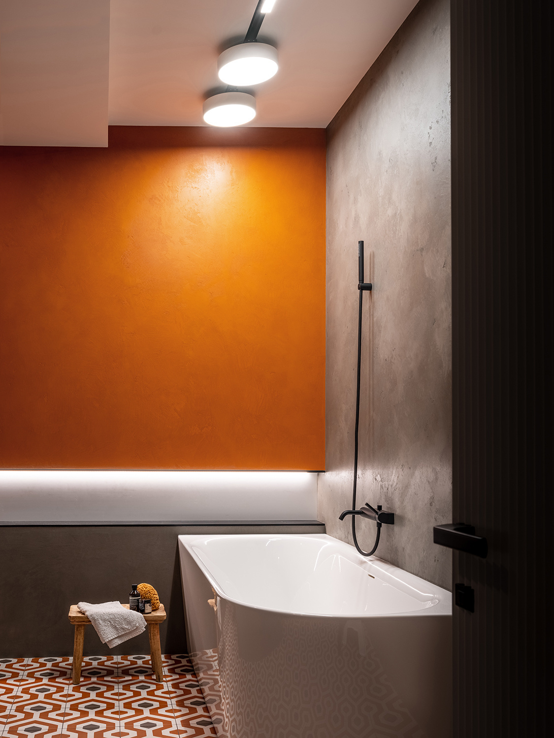 Phòng tắm thường mang đến cảm giác lạnh lẽo, đặc biệt là khi tường bê tông xám kết hợp cửa ra vào màu đen và bồn tắm trắng. Để mang đến sự ấm áp, NTK đã chọn sơn một bức tường màu cam, kết hợp ánh đèn trần nhằm xua đi sự lạnh lẽo trước đó.
