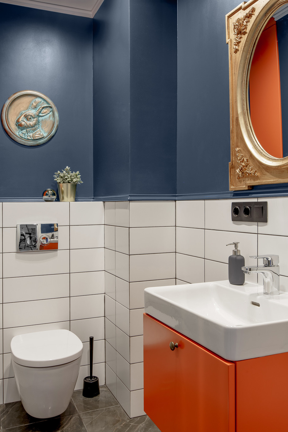 Phòng tắm tuy nhỏ nhưng NTK khéo léo kết hợp sơn tường màu xanh navy đậm và gạch ốp màu trắng để trang trí nội thất. Bên cạnh đó, chiếc tủ vanity (tủ lưu trữ kết hợp bồn rửa) màu cam và trắng sứ càng làm tăng sự nổi bật cho phòng tắm.