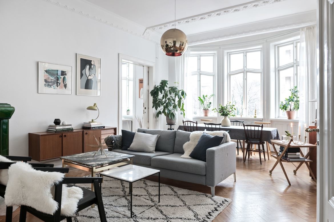 Phòng khách trong căn hộ tại Helsingborg (Thụy Điển) mang đến cảm giác tươi sáng, rộng rãi, mặc dù diện tích thật khá 'khiêm tốn'. Sơn tường trắng kết hợp với màu xám của sofa và chiếc đèn thả trần màu vàng đồng tạo điểm nhấn tuyệt đẹp.