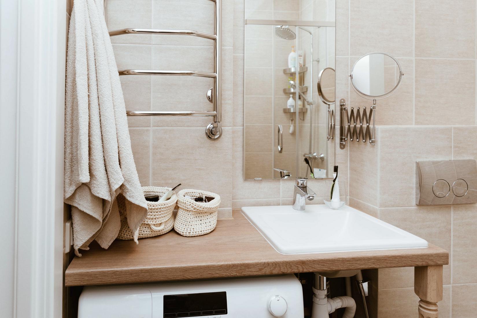 Mặt bàn gỗ kết hợp bồn rửa tay nhỏ gọn, bên trên là tấm gương treo dọc tường giúp phản chiếu không gian phòng tắm. Một chiếc máy giặt được bố trí gọn gàng ngay dưới mặt bàn giúp tiết kiệm diện tích.