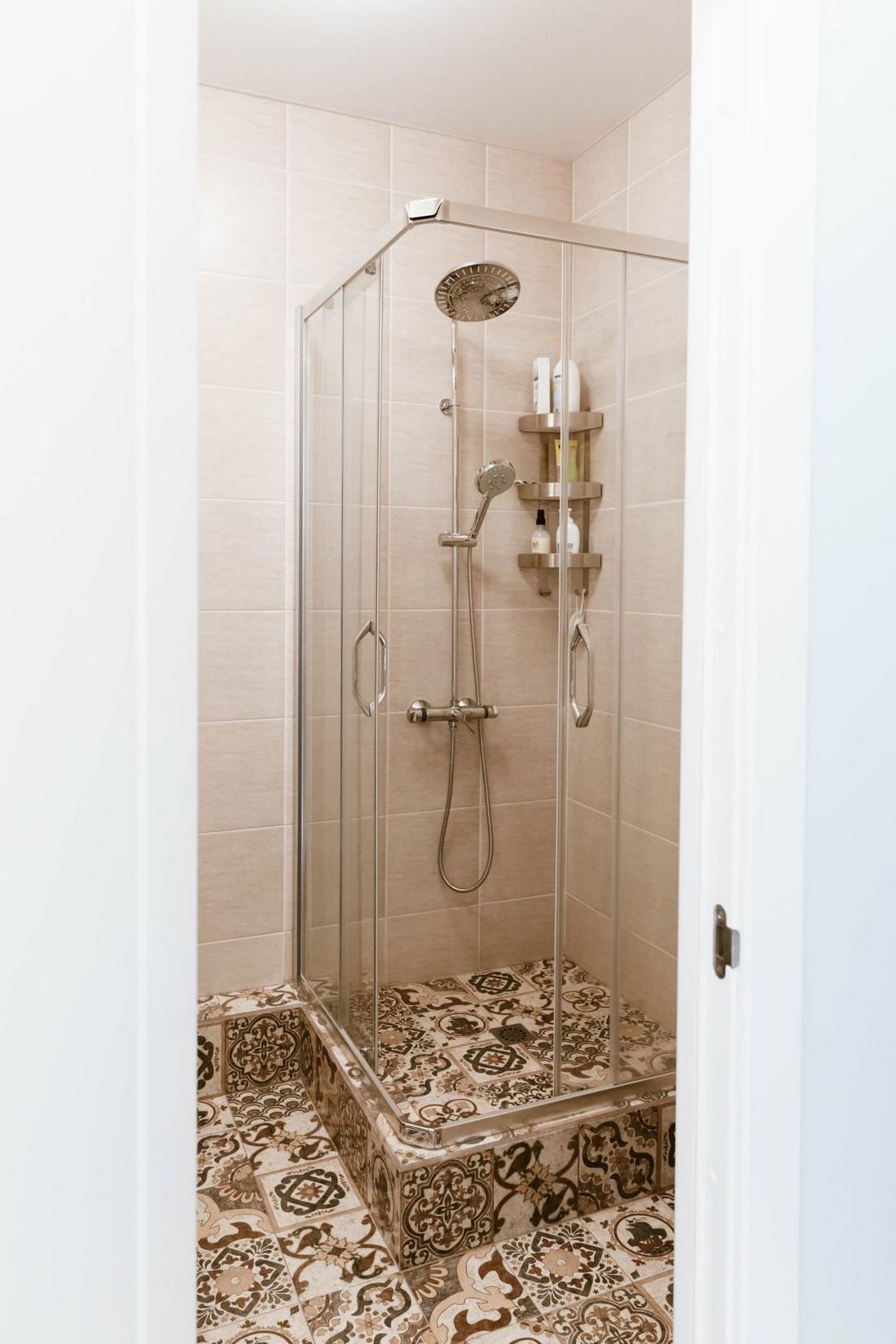 Phòng tắm sử dụng gạch lát tường màu be cho cảm giác sang trọng. Riêng phần sàn lát gạch bông hoa văn cổ điển để tạo điểm nhấn. Buồng tắm đứng thiết kế nâng sàn khoảng 20cm với hệ thống thoát nước, vòi hoa sen và kệ mở gắn tường tiện ích.