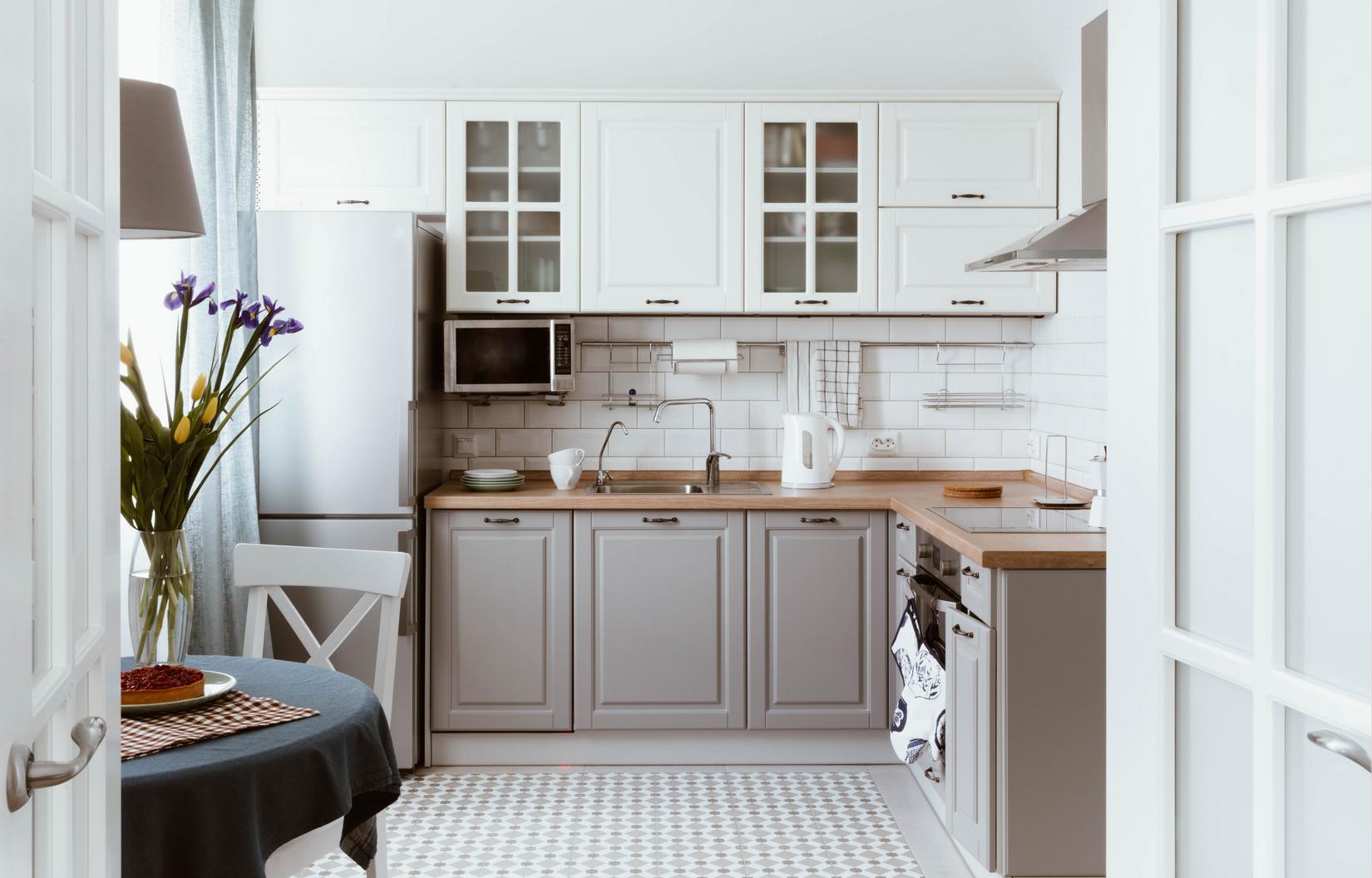 Sàn phòng bếp được lát gạch tương tự nhằm tạo sự liên kết với hành lang lối vào. Tủ bếp trên màu trắng tương phản nhẹ nhàng với tủ bếp dưới màu xám, mặt bàn bếp ốp gỗ cũng tạo nên vẻ mộc mạc cho phòng bếp nhỏ.