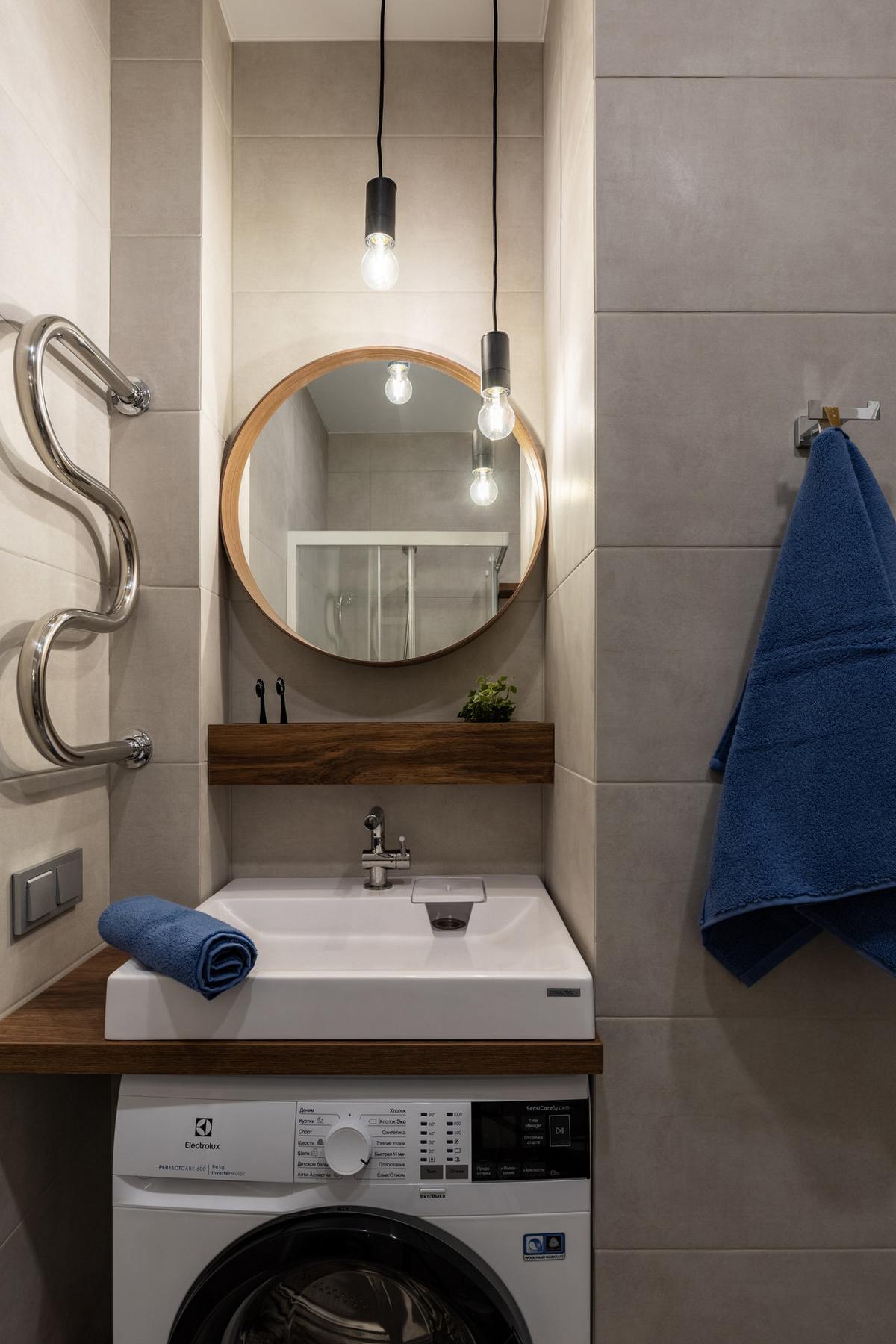 Khu vực phòng tắm nhỏ gọn với bồn rửa, kệ và gương soi bố trí trong hốc tường nhỏ gọn. Máy giặt nhỏ sắp xếp bên dưới bồn rửa, những dây đèn thả trần phá trước gương soi cũng góp phần 'nhân đôi' ánh sáng.