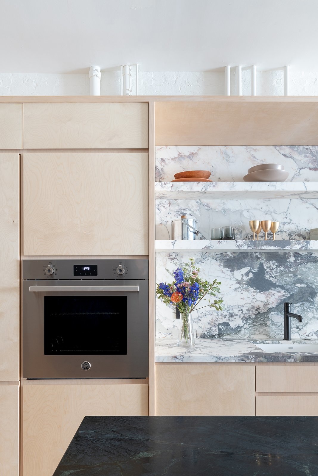 Phòng bếp do GLAM Studio thiết kế với sự kết hợp của hai vật liệu là ván ép cho hệ thống tủ lưu trữ và đá cẩm thạch. Sự mộc mạc, tươi sáng của gỗ nhạt màu với nét sang trọng của đá xám - trắng khiến căn bếp tinh tế vô cùng.