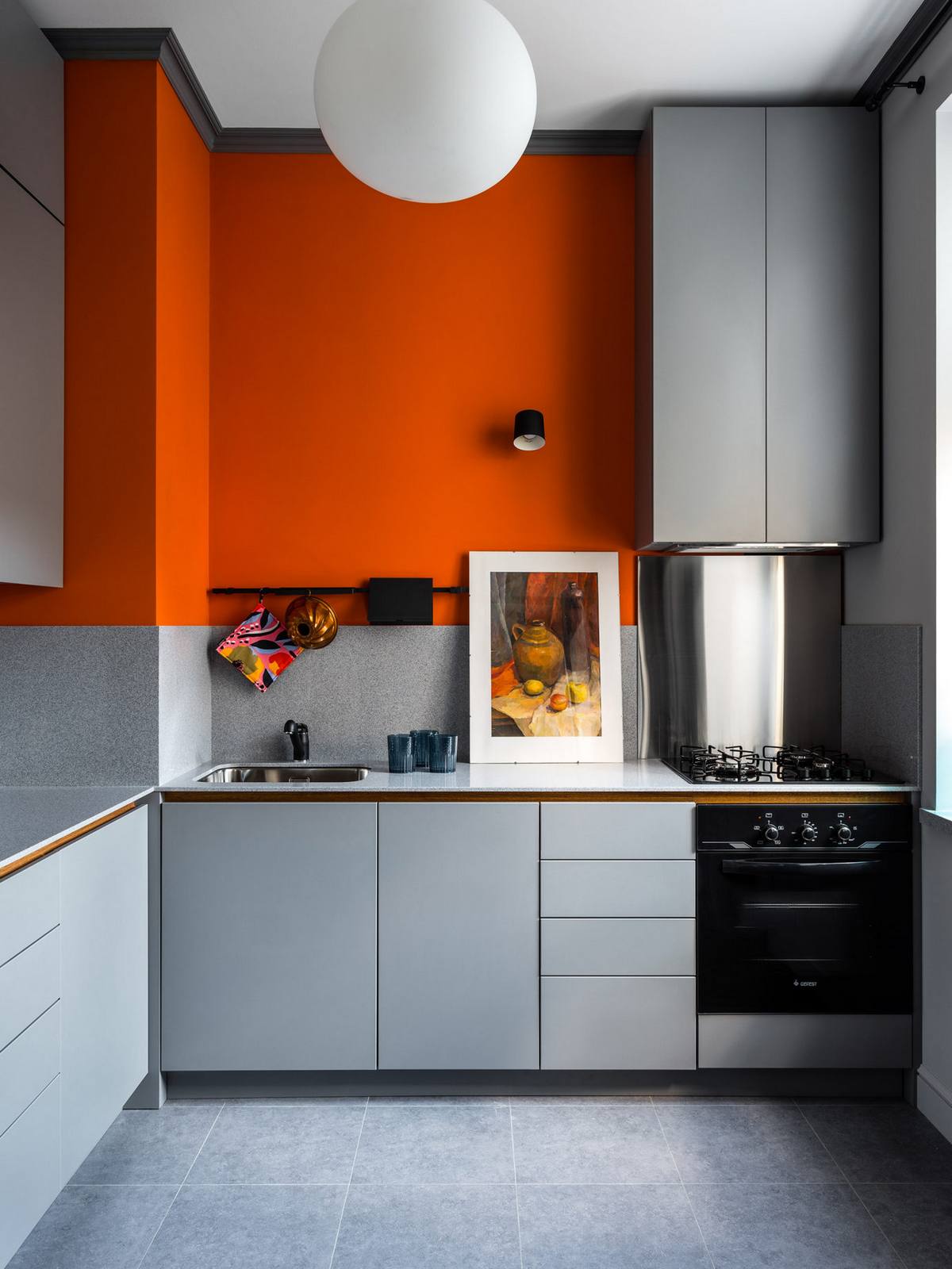 NTK lựa chọn thiết kế tủ bếp chữ L để phù hợp với cấu trúc của căn hộ nhỏ, vừa đảm bảo sự thuận tiện cho người đứng bếp khi thao tác. Bên cạnh gam màu xám chủ đạo, chúng ta nhanh chóng bị thu hút bởi sơn tường màu cam nồng nàn, tươi trẻ.