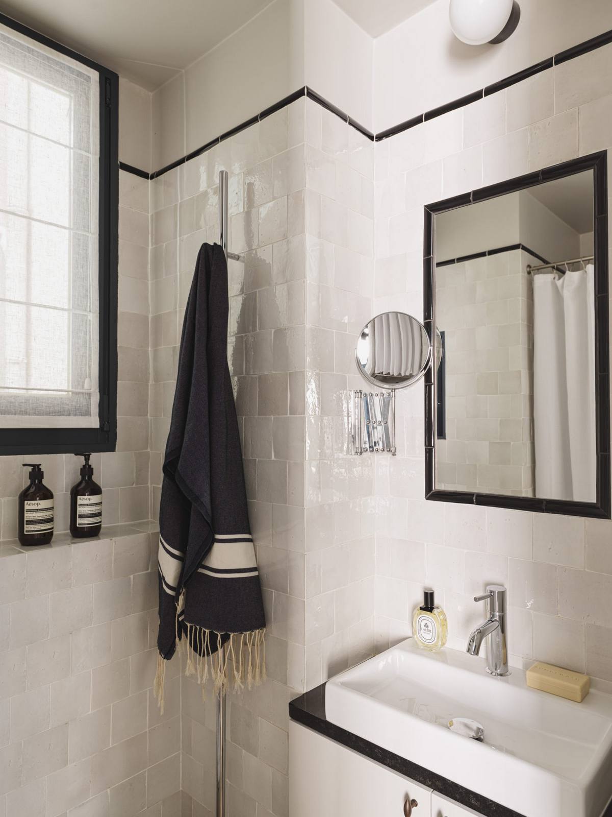 Phòng tắm nhỏ sử dụng gam màu trắng với các chi tiết màu đen làm điểm nhấn cho vẻ đẹp cổ điển. Cửa sổ phòng tắm tích hợp lớp rèm che mờ để tạo sự riêng tư. Gạch ốp tường sáng bóng cùng gương soi cho không gian tươi sáng và rộng rãi hơn so với diện tích thật.