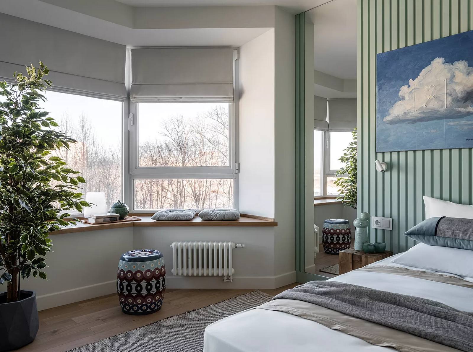 Phòng ngủ với cửa sổ được tận dụng làm khu vực “chill”, nhìn ra khung cảnh lãng mạn. Đầu giường được trang trí bởi tranh vẽ trời xanh mây trắng tươi sáng, bên cạnh là tấm gương lớn khổ dọc giúp 'nhân đôi' căn phòng bằng thị giác.