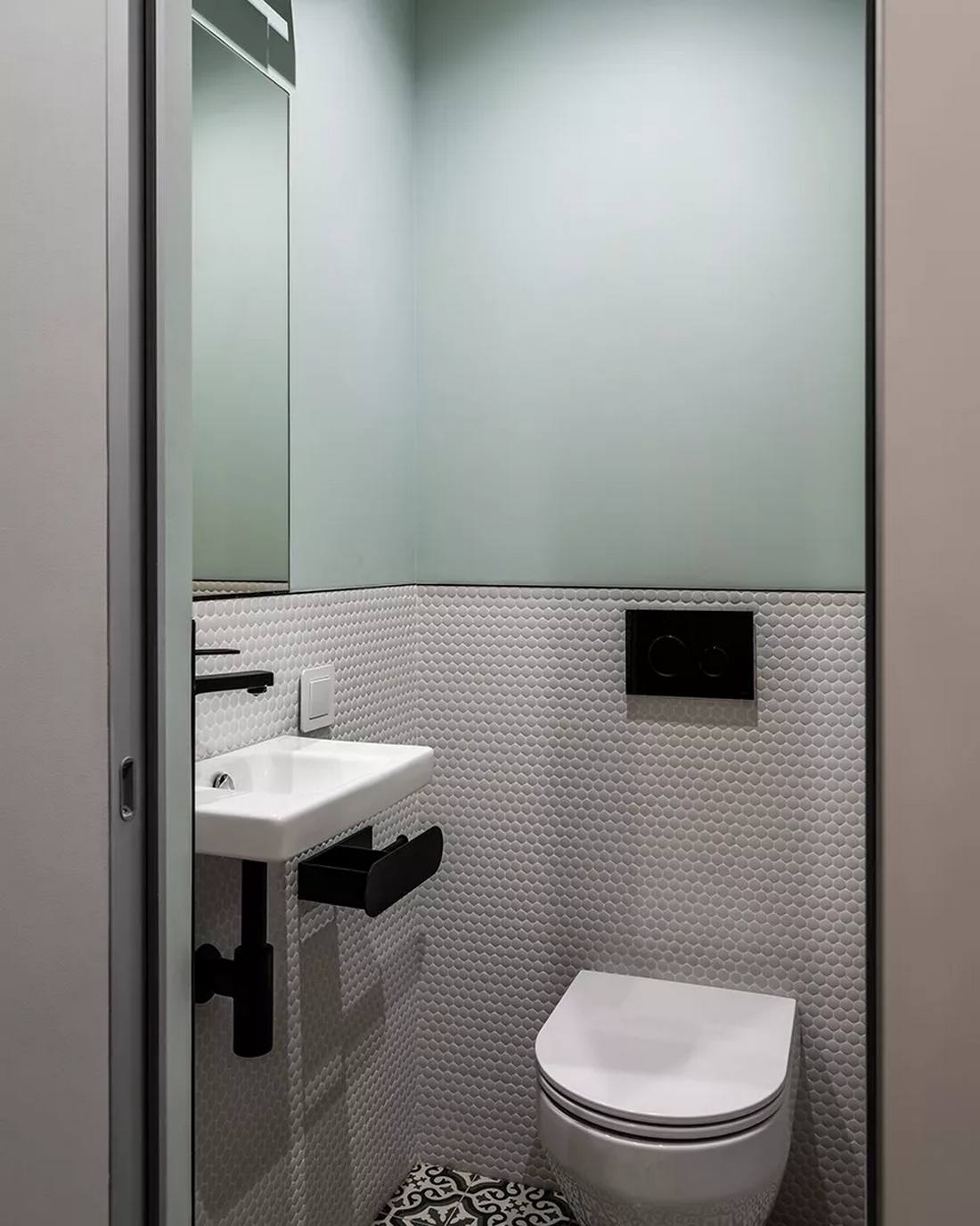 Phòng vệ sinh được trang trí với hiệu ứng bức tường 'chia đôi', phần trên được sơn màu xanh lam mịn mượt, phần dưới là những viên gạch penny hình tròn nhỏ nhắn. Hoa văn gạch lát sàn hoàn toàn tương đồng với hành lang.
