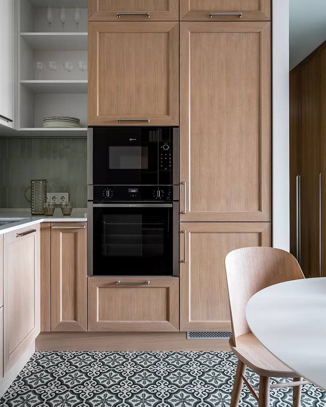 Tủ bếp được thiết kế kiểu chữ L vừa phù hợp với cấu trúc căn hộ vừa tiết kiệm diện tích cho những không gian vừa và nhỏ. Hệ thống tủ gỗ sáng màu tạo sự tương phản nhẹ nhàng với tủ bếp trên màu be và gạch ốp backsplash màu xám nhạt.