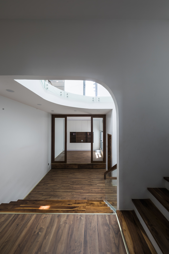Sàn nhà, các bậc tam cấp ốp gỗ màu trầm ấm tạo sự tương phản trên nền tường trắng, mang đến chiều sâu cho ngôi nhà, đồng thời liên kết các tầng với nhau một cách trực quan.