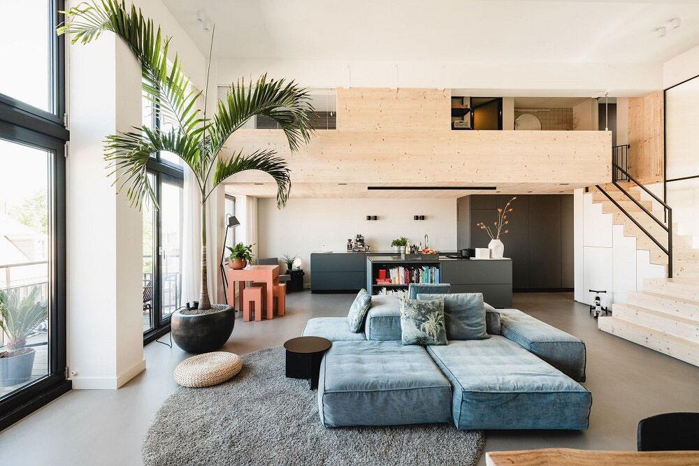 Một chiếc ghế sofa kiểu module màu xanh lam nhạt được đặt tại vị trí trung tâm phòng khách, kết hợp tấm thảm trải sàn hình tròn giúp “khoanh vùng” nơi tiếp khách.