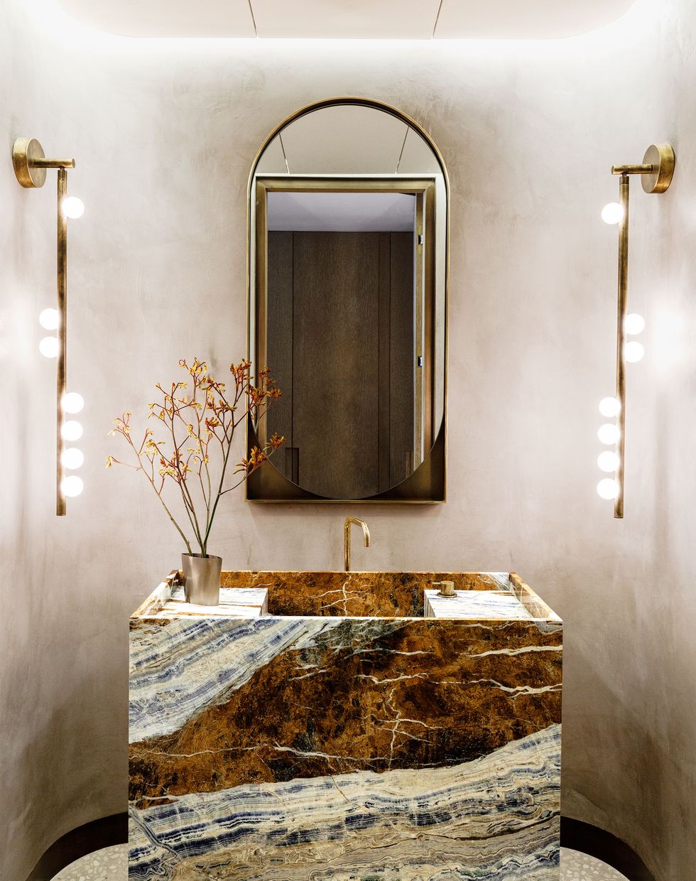 Thiết kế nội thất của phòng tắm này khiến người ta phải trầm trồ bởi sự nổi bật của hệ thống đèn treo tường độc lạ, phản chiếu ánh sáng lấp lánh lên chiếc bồn rửa bằng đá cẩm thạch Cassiopeia cùng vòi rửa mạ vàng đồng màu sang chảnh.