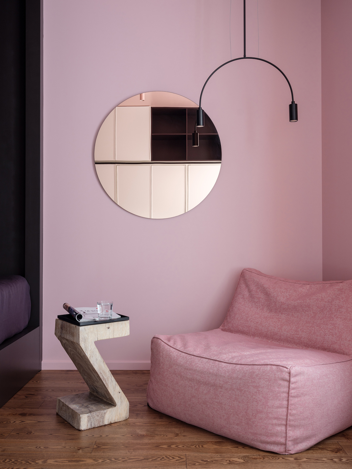Bên ngoài phòng ngủ là góc thư giãn, đọc sách với chiếc ghế màu hồng nhỏ nhắn, êm ái, thiết kế tối giản không tay vịn kèm chiếc bàn hình chữ Z độc đáo. Trên tường treo một tấm gương tròn và đèn thả trần hình vòm cung đẹp mắt.