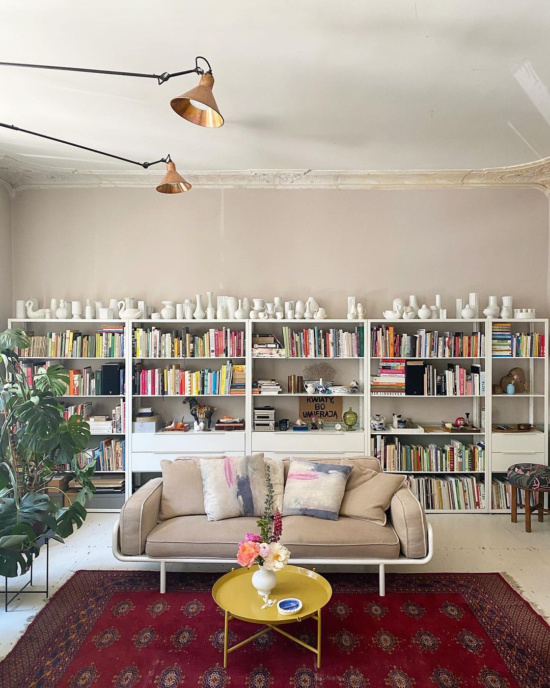 Phòng khách là nơi được chủ nhân bố trí ghế sofa màu be êm ái nổi bật trên tấm thảm trải sàn họa tiết cùng sắc đỏ mận nổi bật. Phía sau là kệ lưu trữ hoành tráng với rất nhiều sách, tạp chí cũng như bộ sưu tập đồ trang trí của cả hai.