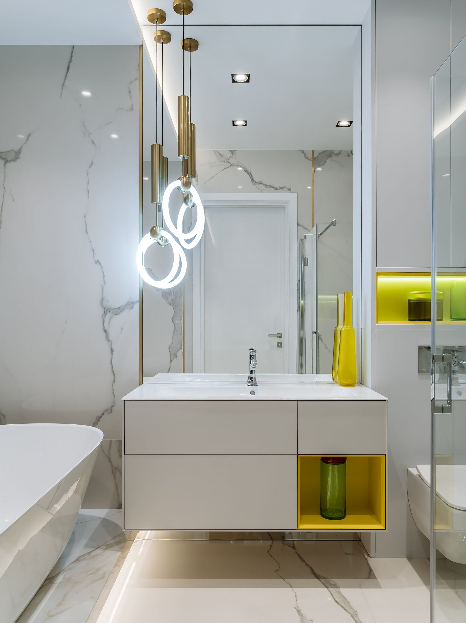 Không gian phòng tắm với gương ốp 'full' tường giúp 'nhân đôi' diện tích hiệu quả. Hệ thống đèn thả trần lấp lánh, đá cẩm thạch sang trọng và chút nhấn nhá của sắc vàng tươi tại hộc tủ lưu trữ, hốc tường trên toilet và chiếc bình trang trí bắt mắt.