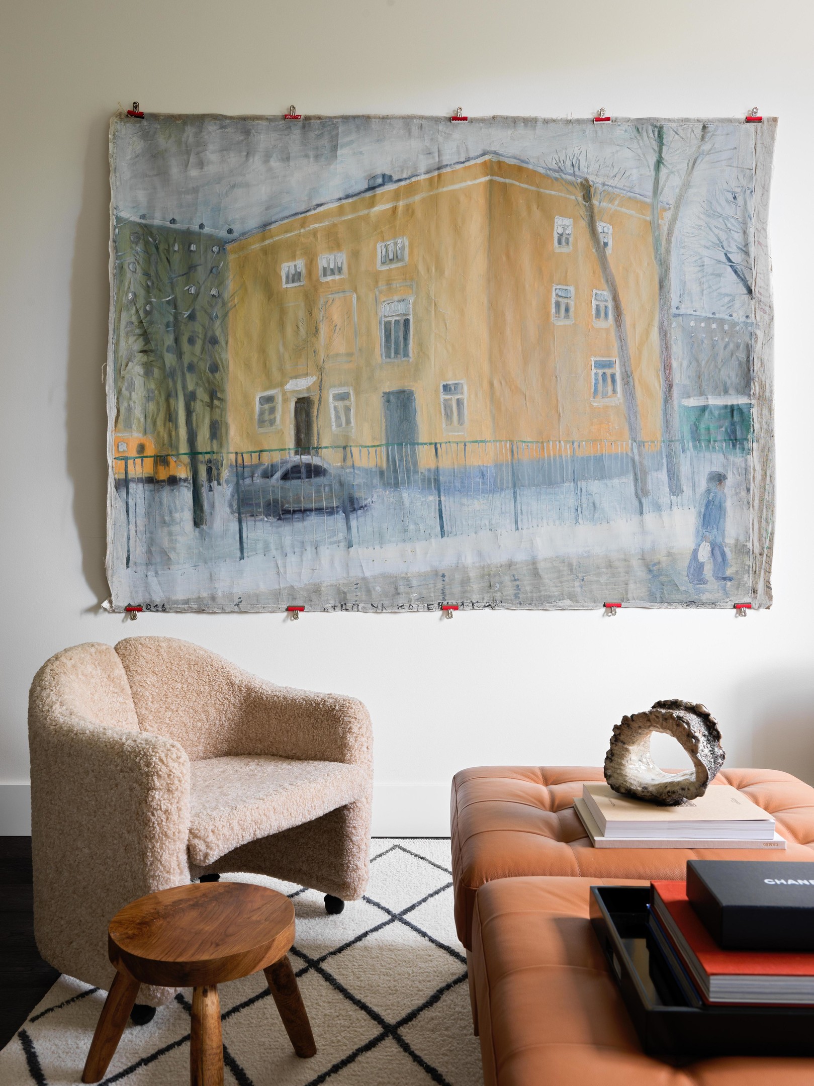 Bên cạnh ghế sofa, hai chiếc ghế đôn được ghép lại cạnh nhau tạo thành bàn nước bọc da màu nâu đậm sang trọng, càng dùng lâu càng đẹp. Cặp ghế bành màu be ấm áp với chiếc ghế đẩu bằng gỗ tạo thành chiếc 'bàn phụ' nhỏ. Tất cả bố trí trên tấm thảm trải sàn mịn mượt. Trên tường là bức tranh của họa sĩ Pyotr Bronfin.