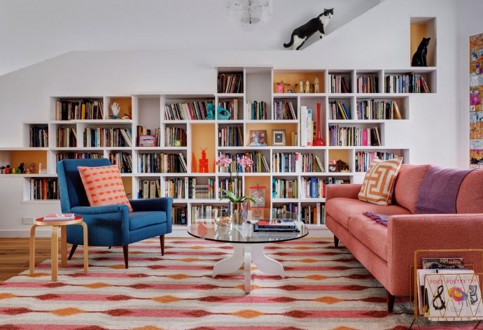 Phòng khách lôi cuốn với gam màu hồng san hô của sofa, thảm trải sàn, sắc xanh coban của ghế bành, và dĩ nhiên là cả hệ thống kệ lưu trữ kết hợp hộc tủ âm tường tạo nên một thư viện mini đẹp xuất sắc!