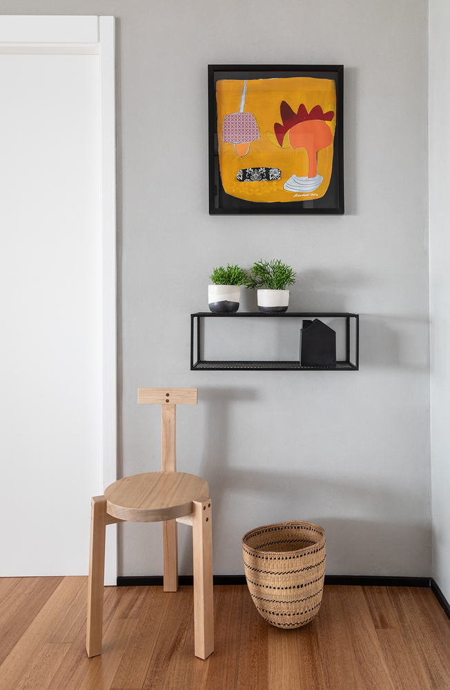 Lối vào căn hộ với bức tranh sắc cam nổi bật trên nền tường xám, chiếc kệ gắn tường màu đen vừa để lưu trữ vừa trang trí vài chậu cảnh tươi xanh. Một chiếc ghế nghỉ chân, một chiếc giỏ đựng đồ - mọi thứ nơi đây đều nhỏ xinh, gọn nhẹ.
