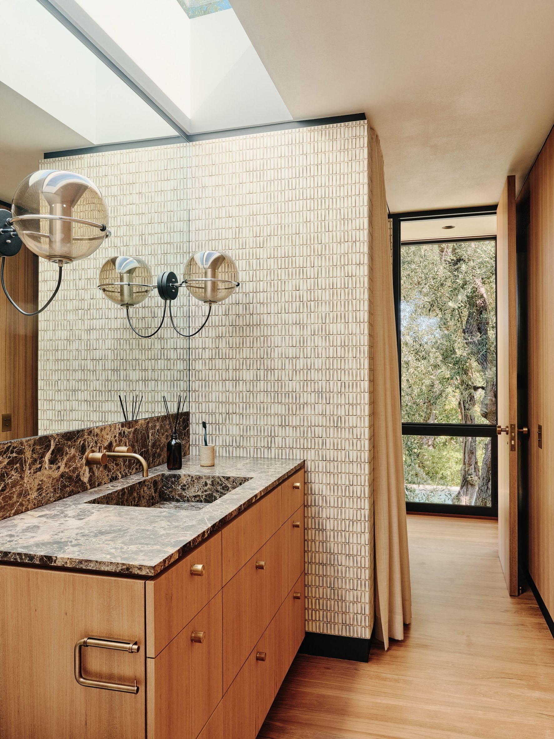 Phòng tắm dành cho khách có mặt bàn bằng đá cẩm thạch sẫm màu và tường ốp bằng gạch sứ Nhật Bản và cặp đèn thả trần hình quả cầu phong cách cổ điển.