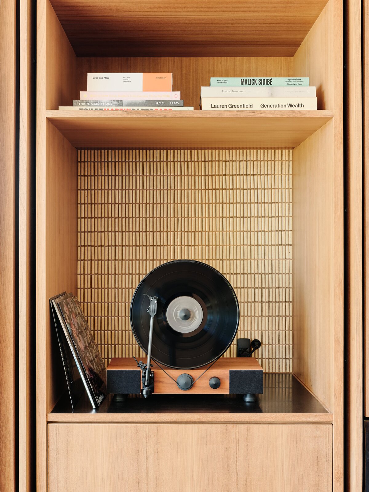 Một hệ thống giá đỡ cao từ trần đến sàn chứa các hốc để sách, đồ uống cocktail và máy phát nhạc đĩa than phong cách cổ điển của chủ nhân. 