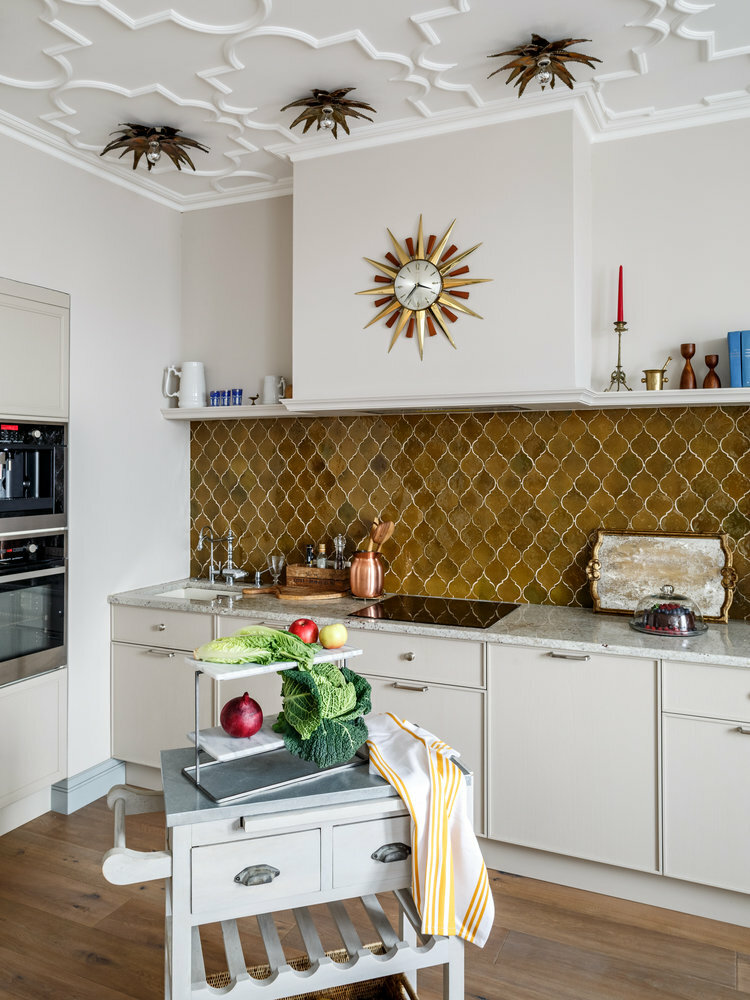 Phòng bếp do Nadya Zotova thiết kế, gây ấn tượng bởi trần nhà với phào chỉ họa tiết đẹp mắt cùng đèn ốp trần bắt mắt. Backsplash ốp gạch màu vàng đồng ấm áp cùng họa tiết gợi nhớ đến kiến trúc của đất nước Maroc.