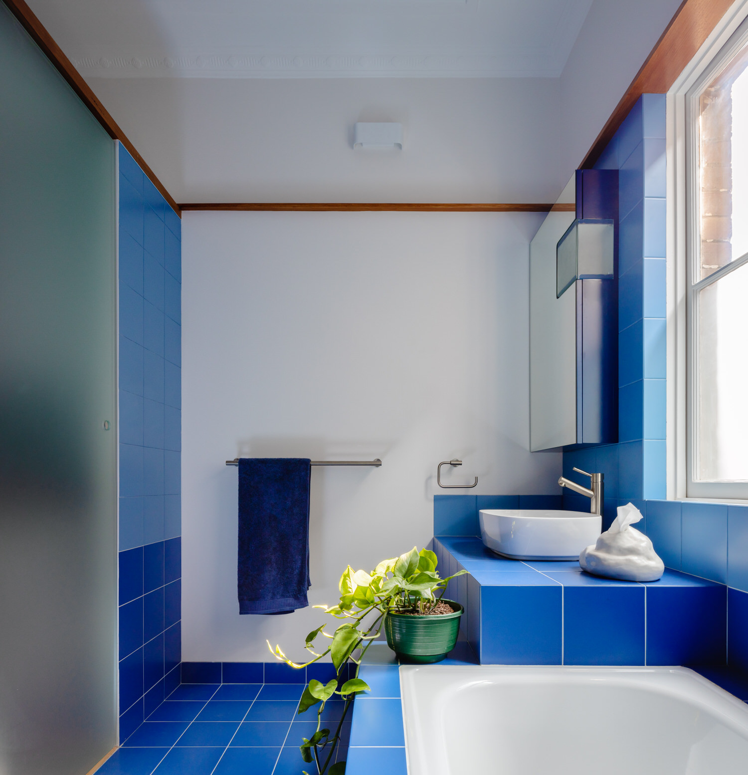 Phòng tắm với những chi tiết màu xanh lam đậm như sơn tường, gạch ốp lát, bồn rửa mặt, khăn tắm,... tạo sự nổi bật trên phông nền trắng chủ đạo.