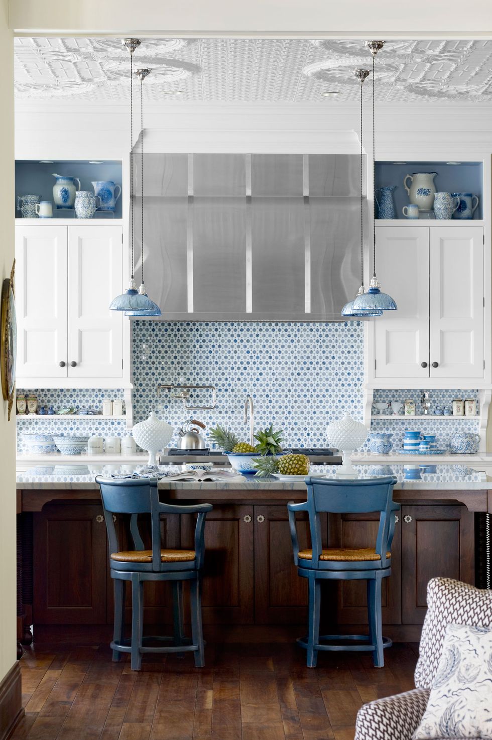 Gam màu xanh lam trong ý tưởng trang trí phòng bếp này được sử dụng rất tiết chế nhưng phân bố hài hòa, bao gồm: Hốc tường phía trên tủ bếp, backsplash, đèn thả trần và cặp ghế ngồi phong cách cổ điển sang trọng.