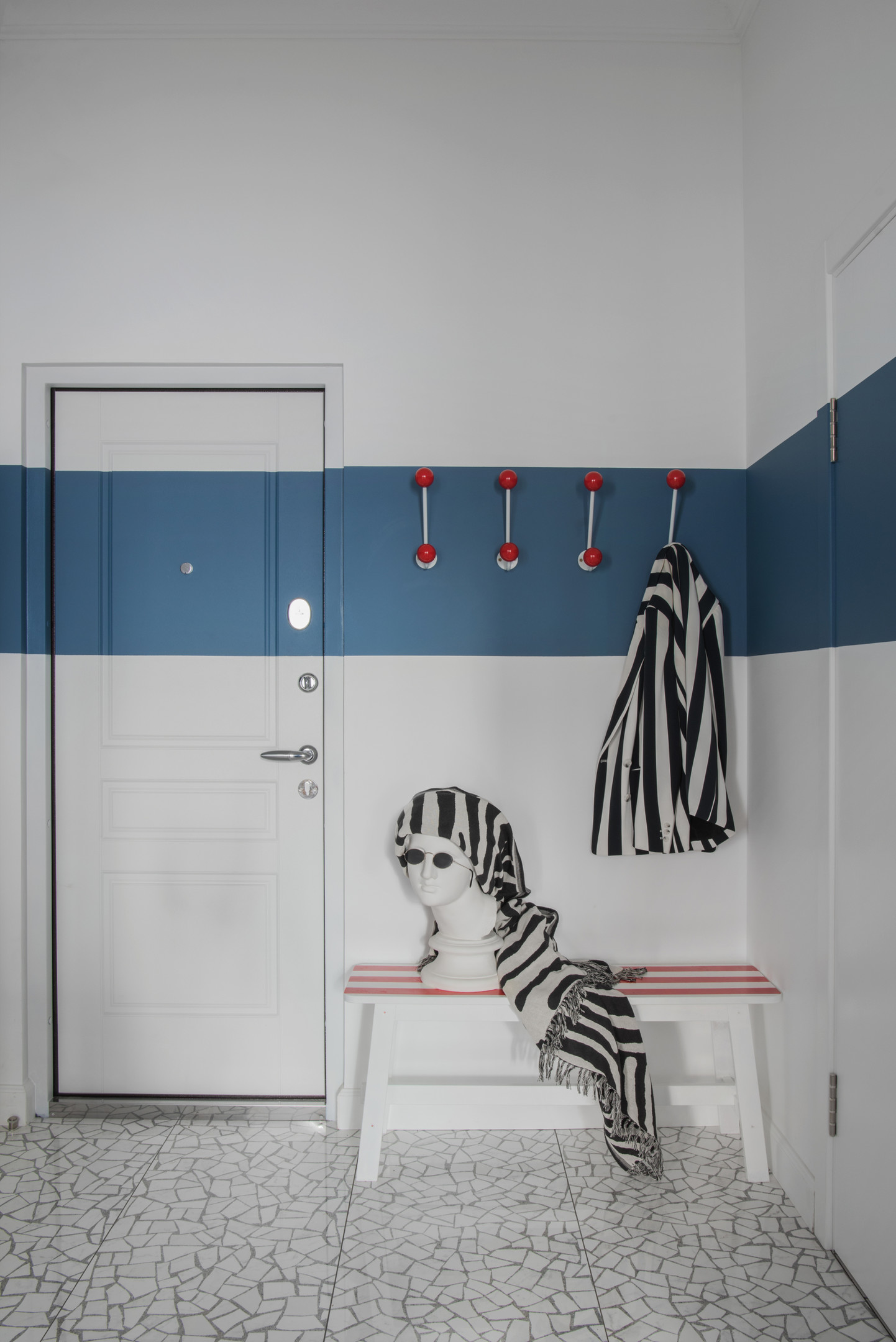 Lối vào căn hộ sử dụng màu xanh lam đậm và trắng để sơn tường, sàn lát đá ấn tượng, thêm vào băng ghế dài từ thương hiệu IKEA được NTK sơn lại những sọc kẻ trắng - hồng. Chiếc áo khoác và khăn choàng họa tiết ngựa vằn trông chất cực kỳ!