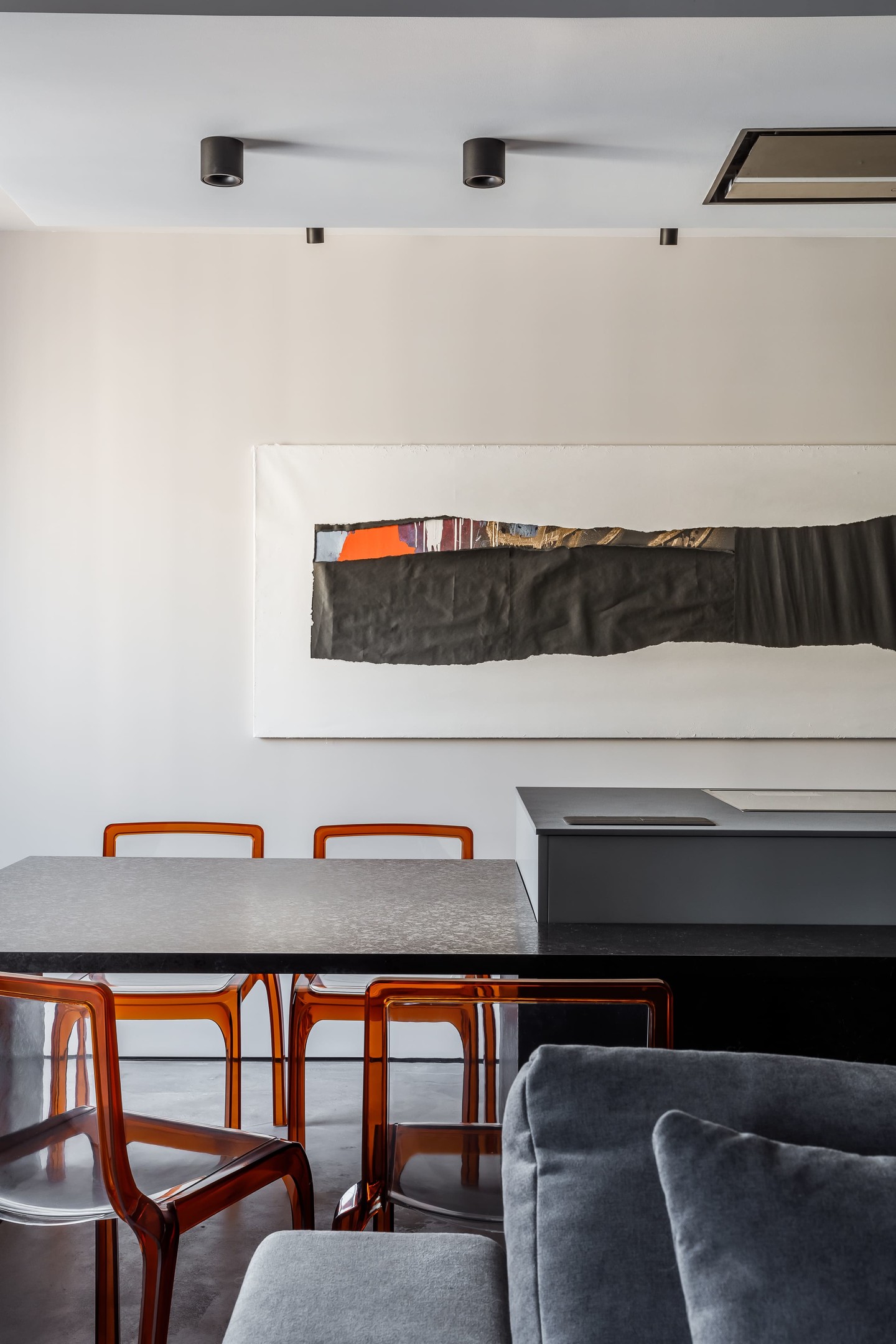 Phòng ăn bố trí ngay sau lưng ghế sofa, ở vị trí vuông góc với phòng bếp. Thiết kế bàn hình chữ nhật tối giản, nổi bật những chiếc ghế nhựa acrylic màu cam đẹp mắt. Trên bức tường cũng được trang trí một tác phẩm nghệ thuật trừu tượng độc lạ.