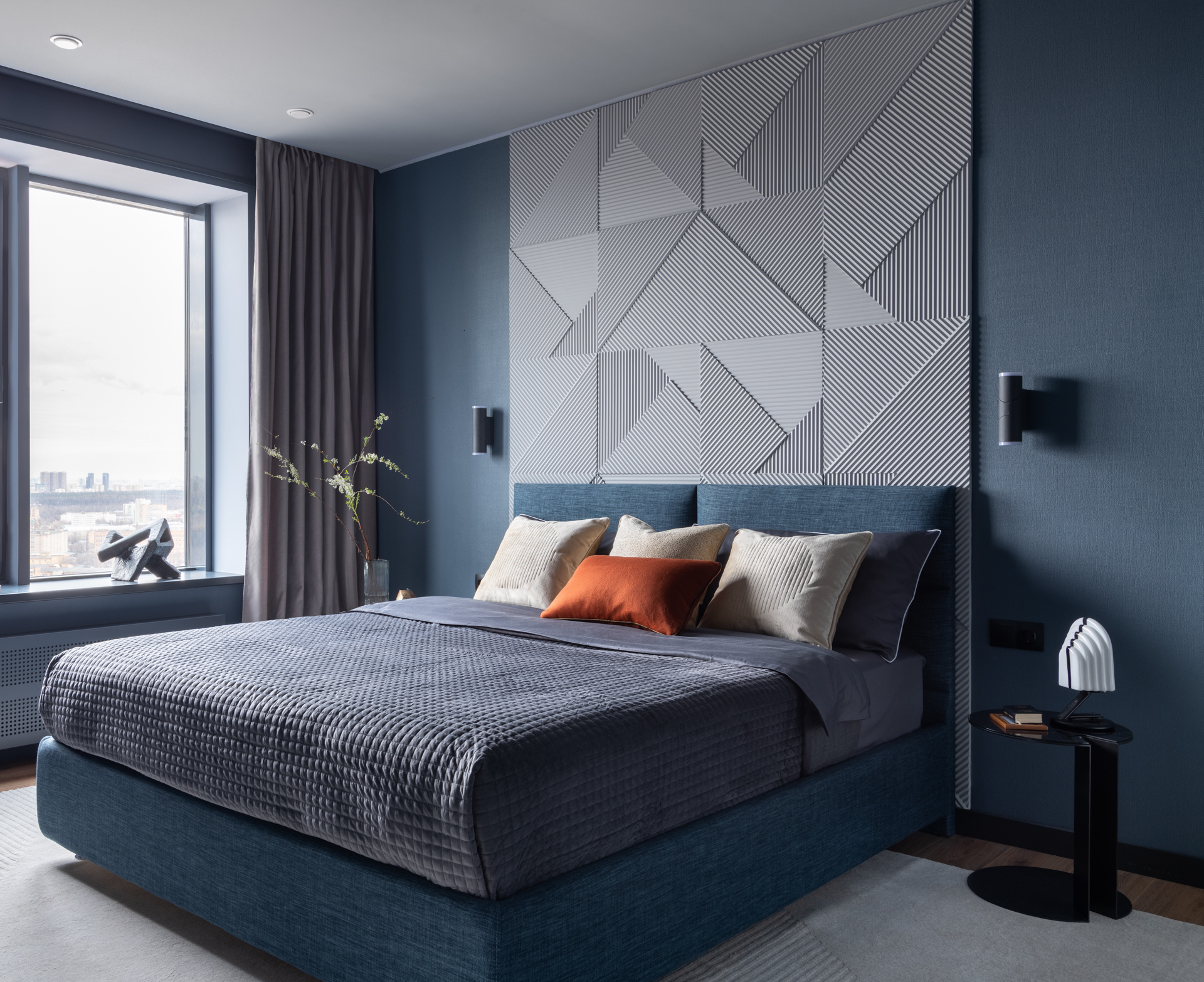 Phòng ngủ của cặp đôi được bày trí tinh tế với rất ít màu sắc, chỉ sử dụng tone xanh lam và xám chủ đạo như phong cách thiết kế tổng thể. Một chiếc gối màu cam gạch được xem là tone màu nóng duy nhất trong căn phòng. 