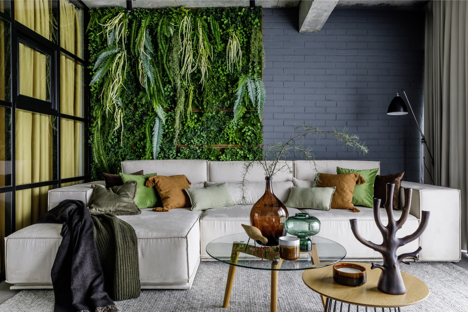 Phòng khách thiết kế theo phong cách Organic với tường gạch sơn màu xanh lam đậm, nội thất gỗ mộc mạc. Ghế sofa cỡ lớn tuy sử dụng gam màu trắng nhưng vẫn không bị nhạt nhòa nhờ 'khu vườn thẳng đứng' làm bức tranh sống động phía sau.