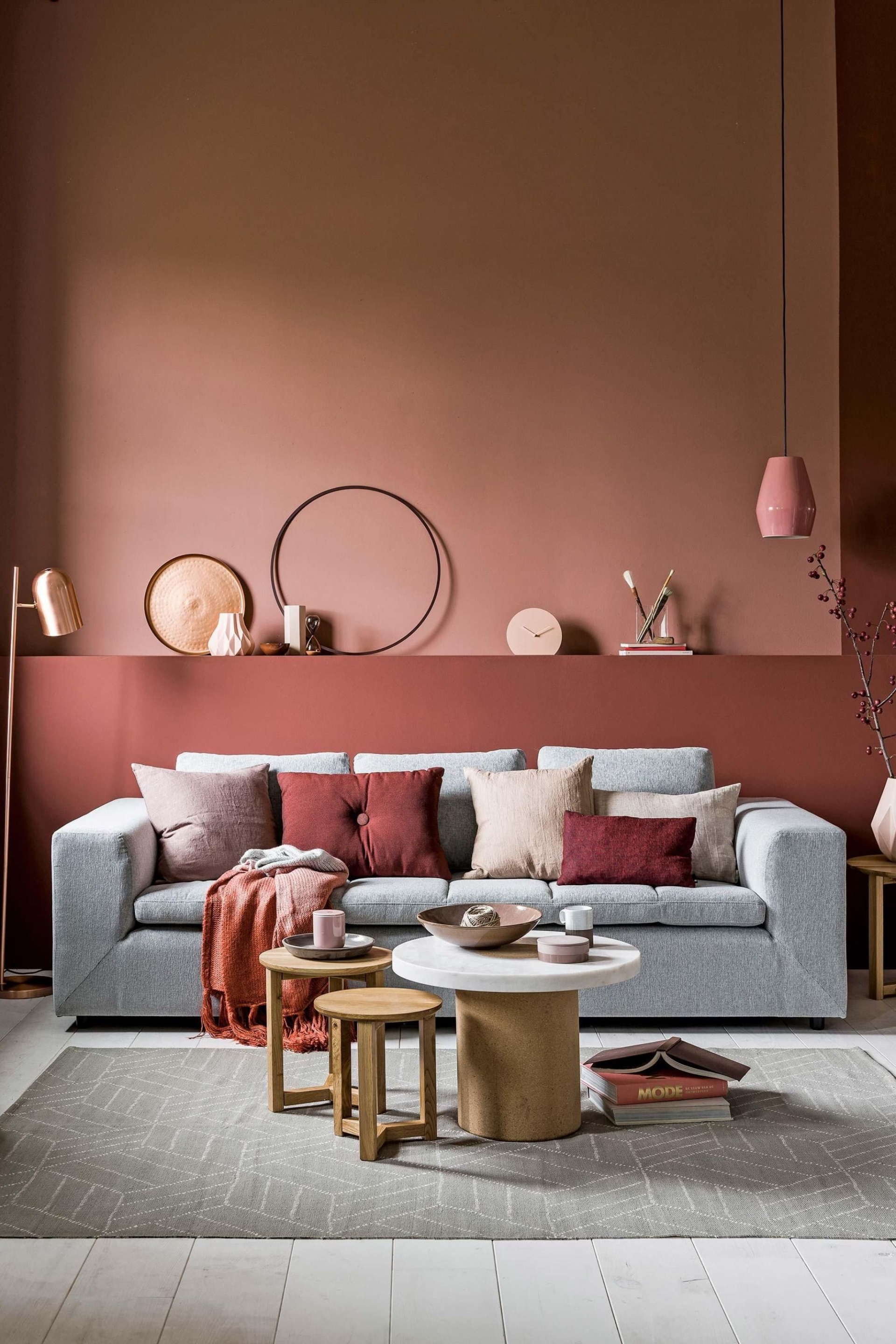 Phòng khách mùa Thu ấm áp với bức tường sơn màu hồng và đỏ tía. Ghế sofa và thảm trải sàn màu xám tương phản nhẹ nhàng, kết hợp với đèn thả trần, lọ hoa, gối ôm và những món đồ gốm sứ với sắc hồng xinh xinh trên bàn nước.