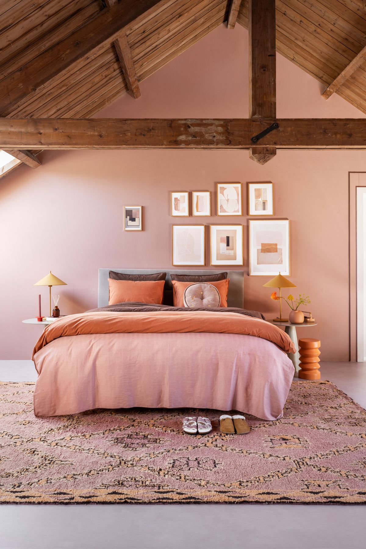 Phòng ngủ trên tầng áp mái với bảng màu cực 'ngọt': Tường hồng phấn, chăn ga gối nâu - cam đất, đèn ngủ sắc vàng mù tạt và tấm thảm trải sàn hồng tím,... tất cả hòa quyện tạo nên bầu không khí ấm cúng, dễ chịu.