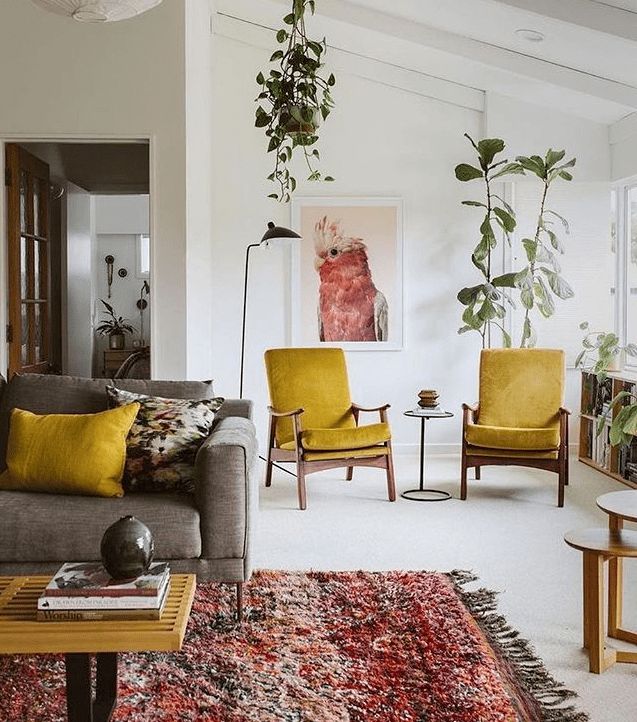 Cặp ghế bành bọc vải nhung vàng mù tạt 'tone sur tone' với gối tựa trên sofa tạo sự liên kết giữa các khu vực nhỏ trong cùng một căn phòng. Sự góp mặt của cây xanh cũng giúp cho sắc vàng trở nên quyến rũ hơn.