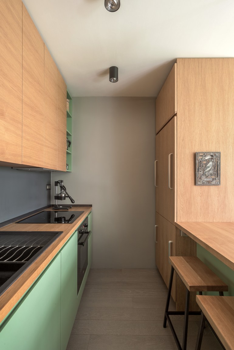Phòng bếp thiết kế kiểu chữ I, là giải pháp hoàn hảo, 'vừa vặn' với bố cục căn hộ cũng như tạo được lối đi thông thoáng ở khu vực nấu nướng.Tủ bếp cũng là sự tưởng phản giữa gam màu xanh lá trẻ trung và gỗ mộc ấm áp.