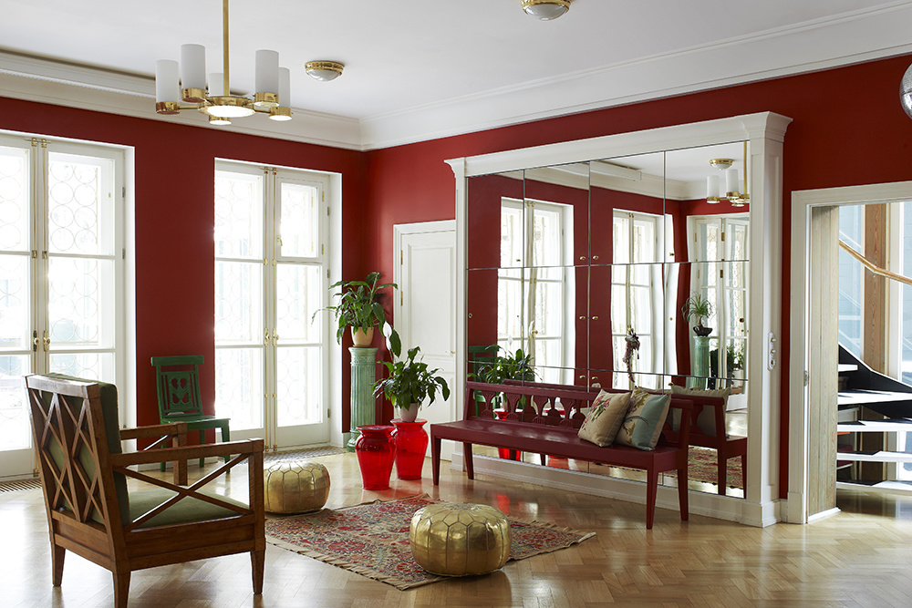Phòng khách mới lạ khi thay sofa bằng một băng ghế gỗ dài sơn màu đỏ mận, những chiếc ghế đôn màu đỏ tươi trong veo cùng bức tường đỏ sang chảnh.