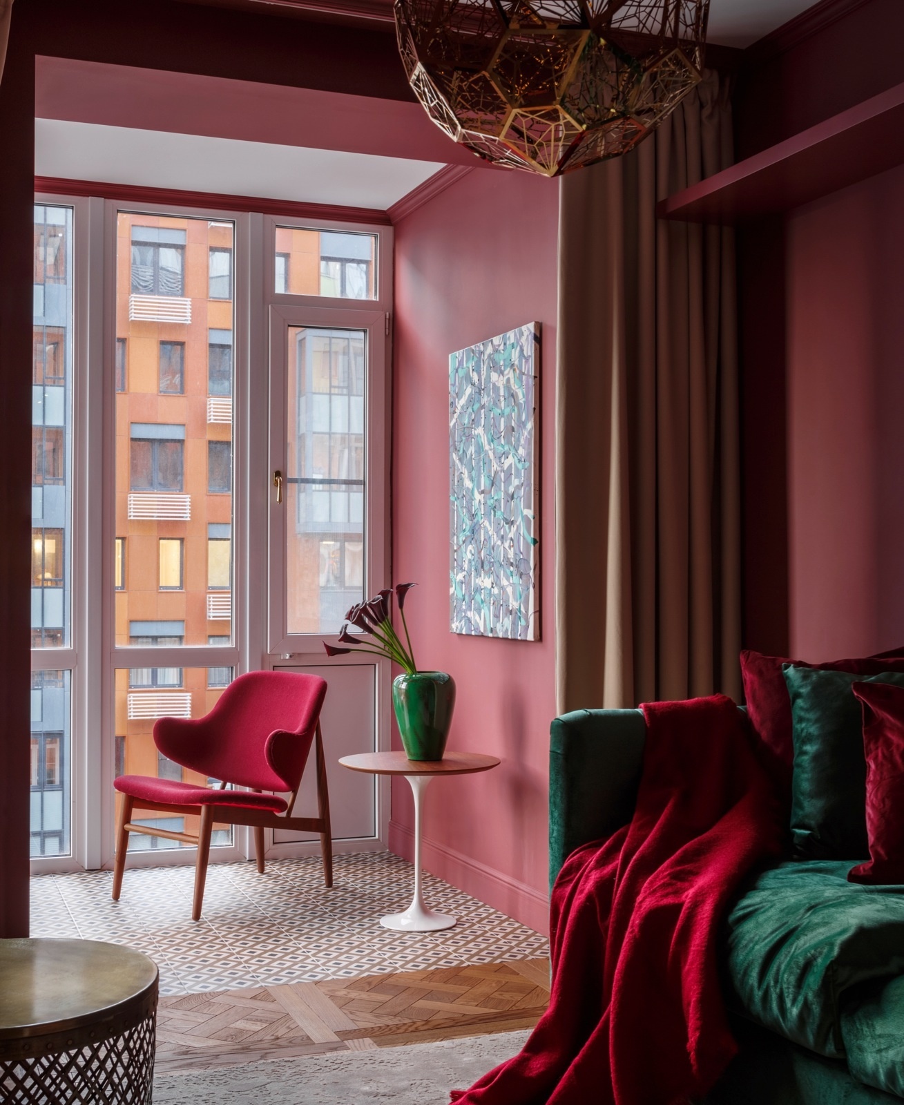 Màu đỏ trầm ấm được sử dụng để kết nối khu vực từ logia vào phòng khách, thêm vào sắc xanh ngọc lục bảo của sofa và lọ hoa trang trí lại càng thêm thời thượng.