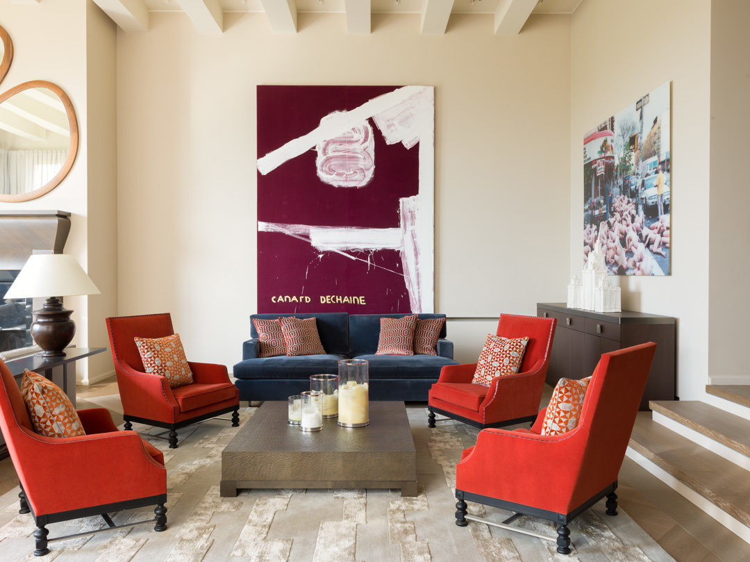 Phòng khách rộng rãi với ghế sofa màu xanh lam đậm ở vị trí trung tâm, thế nhưng mọi sự chú ý đều đổ dồn vào bộ 4 ghế bành màu đỏ phong cách cổ điển xung quanh.